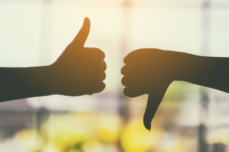 Silhouette image of two hands making thumbs up and thumbs down sign